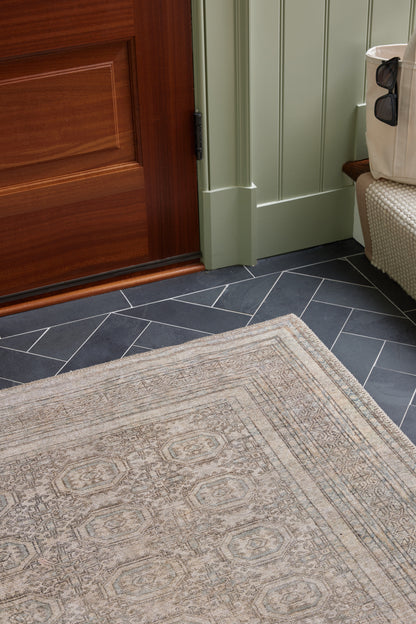 Beige patterned area rug on dark blue-gray tile floor near a wooden door and green paneled wall.