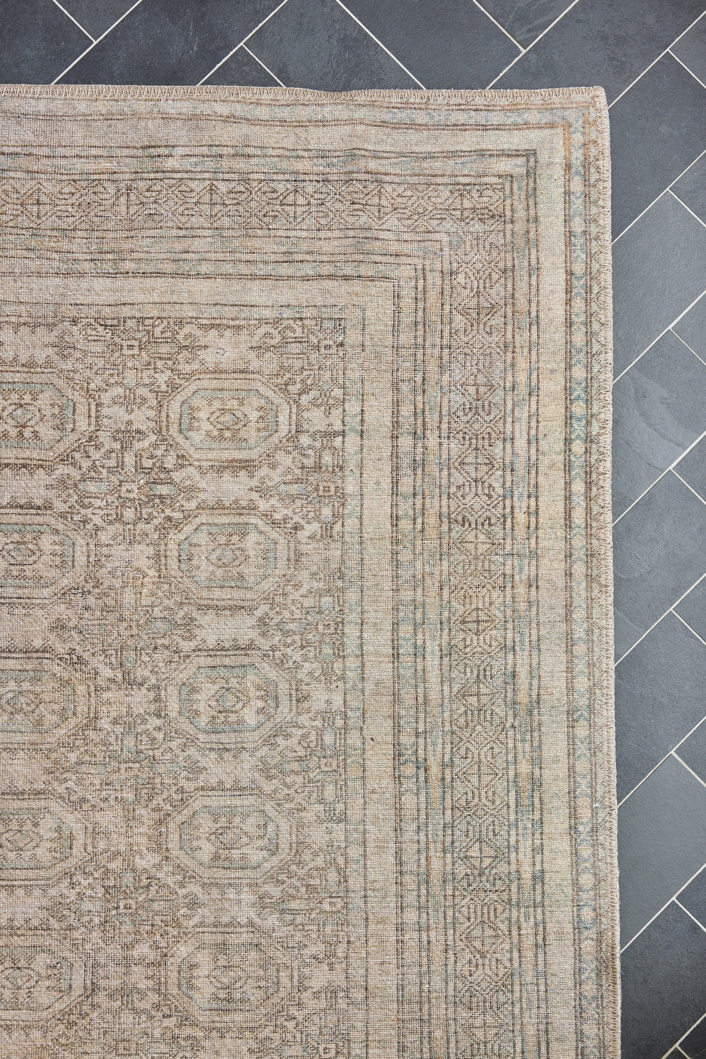 Beige oriental rectangular area rug with faded medallion motifs and multiple border bands on a dark tile floor.