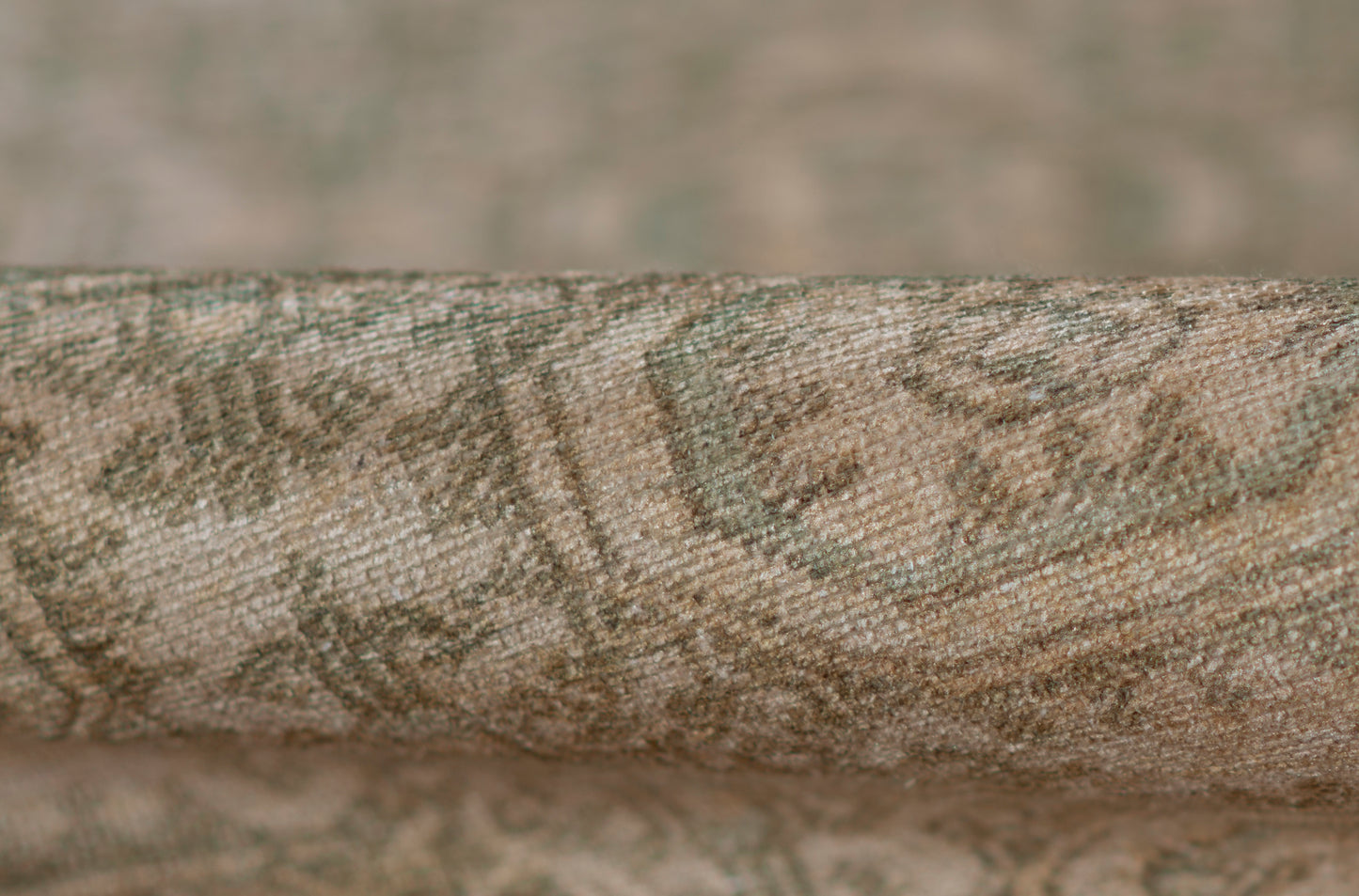 Close-up of a rolled woven rug in beige, brown and sage green with a subtle damask pattern.