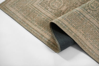 Beige geometric patterned woven rug with muted green accents, folded to reveal dark backing.