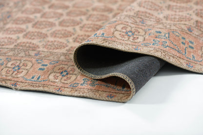 Beige oriental rug with blue geometric motifs, woven textile, folded to show dark backing; traditional style.