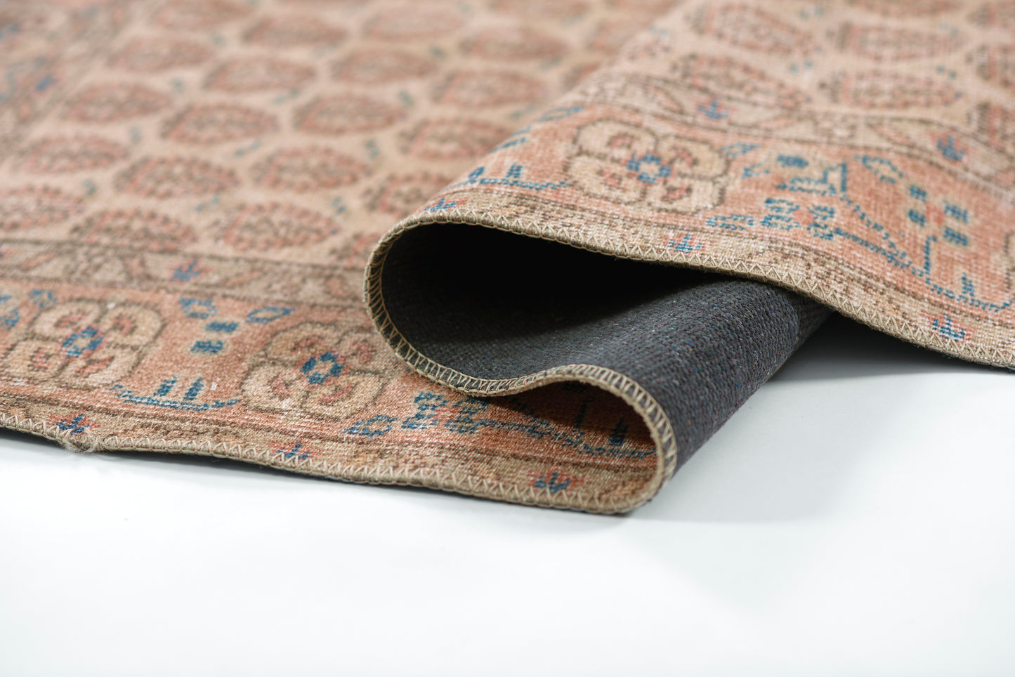 Beige oriental rug with blue floral motifs, folded to show dark backing; woven floor rug for living spaces.