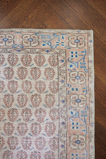 Beige oriental rug with pink teardrop motifs and light blue border patterns on a dark wood floor