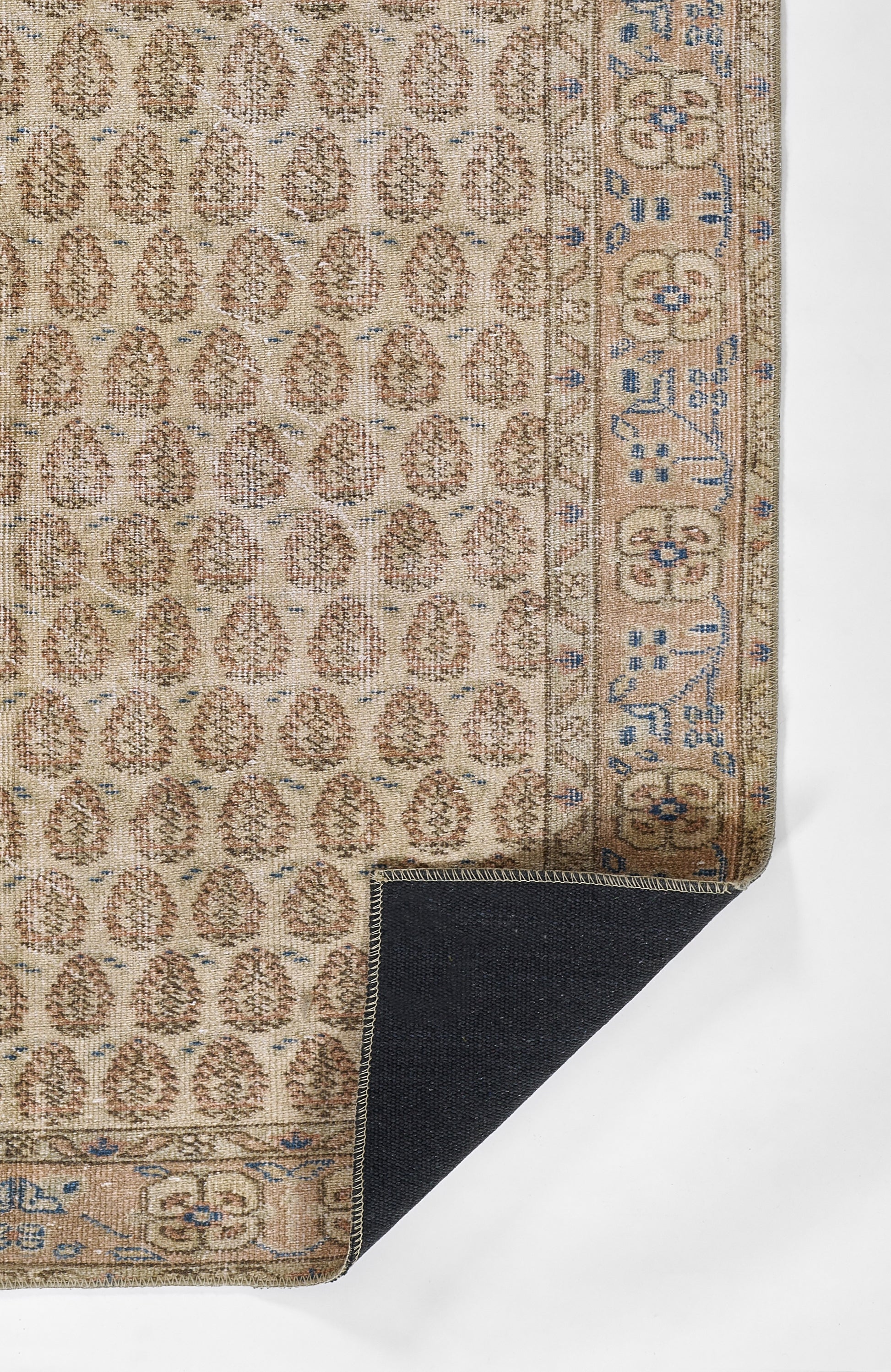 Beige woven oriental rug with brown repeating medallions and blue border; folded corner shows dark backing.