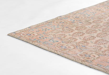 Beige-pink oriental rug with blue and brown geometric floral motifs, woven flat-weave, corner view.