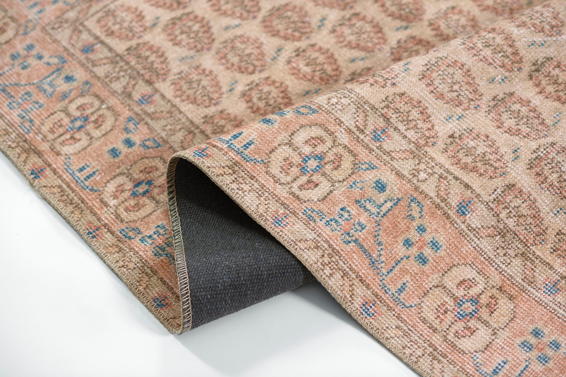 Beige oriental area rug with brown floral medallion pattern and blue accents; rolled corner reveals dark backing.