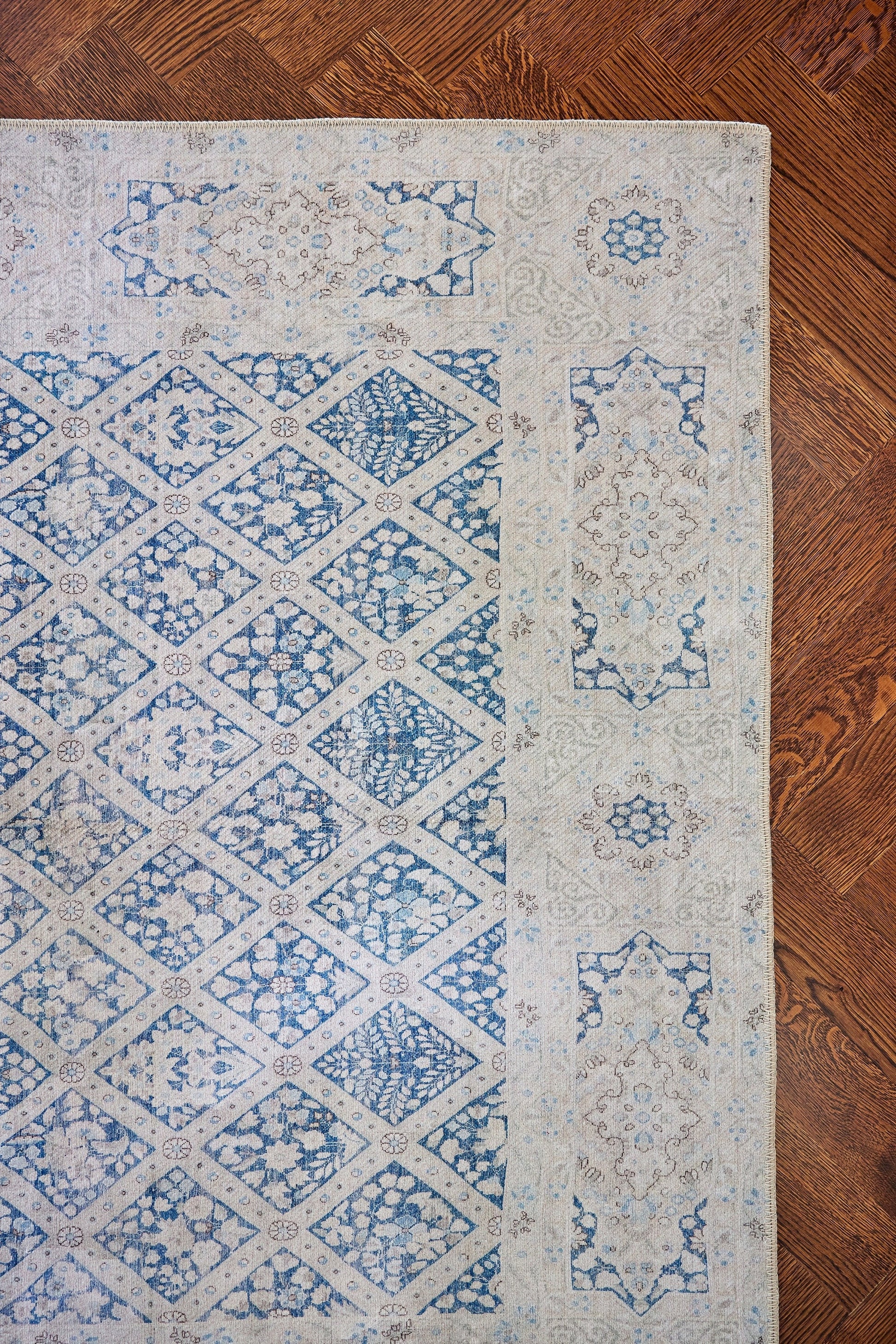 Blue and ivory geometric area rug with diamond lattice pattern and ornate border on wooden floor.