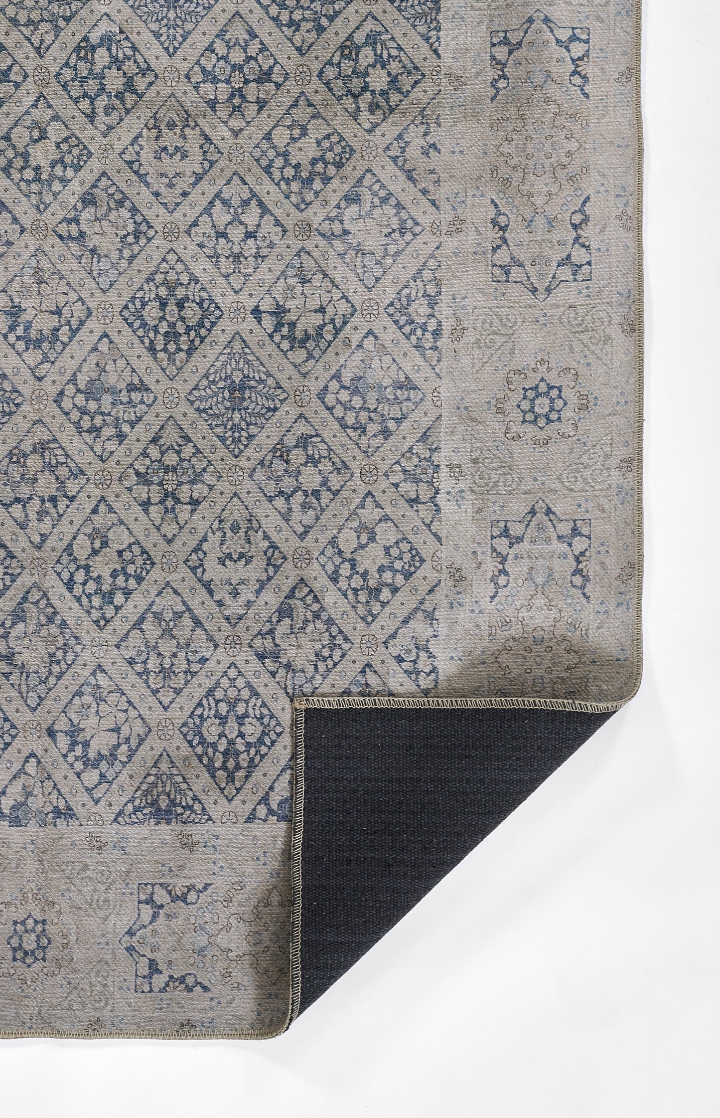 Blue & beige patterned rug with diamond lattice & floral motifs; folded corner showing dark underside.