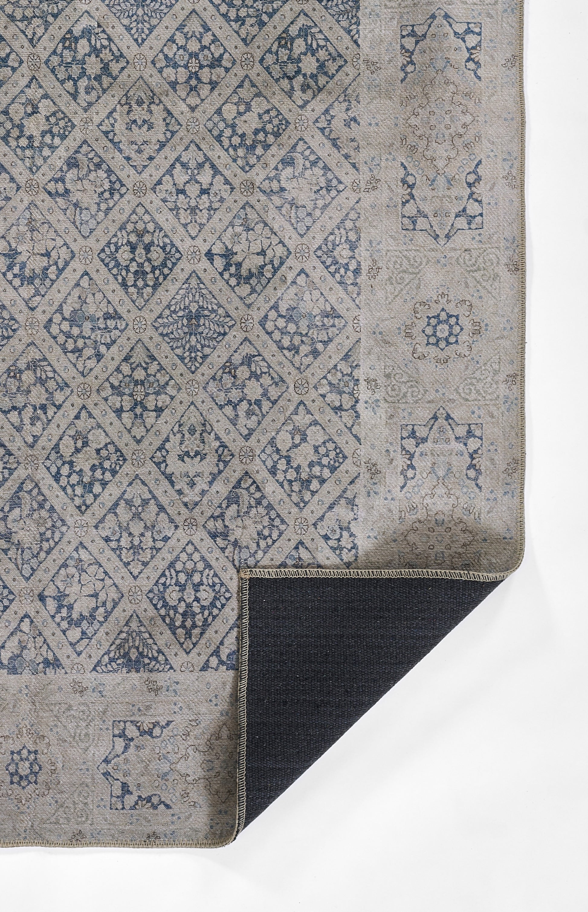 Blue & beige patterned rug with diamond lattice & floral motifs; folded corner showing dark underside.