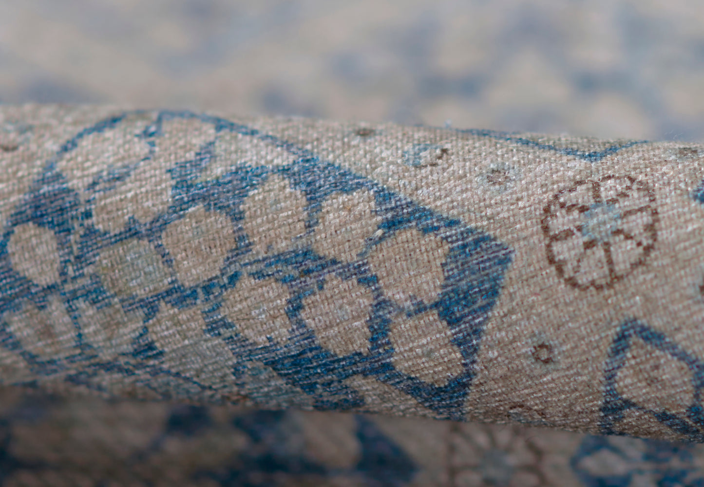 Beige textured woven rug with blue geometric floral print; linen/cotton look; rolled sample for upholstery or decor.