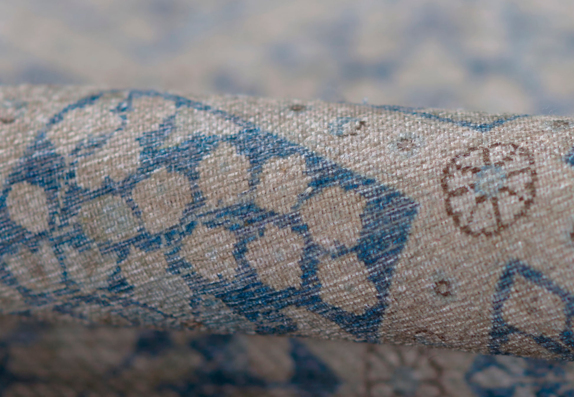 Beige textured woven rug with blue geometric floral print; linen/cotton look; rolled sample for upholstery or decor.