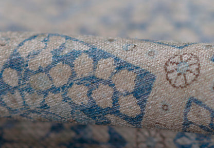 Beige textured woven rug with blue geometric floral print; linen/cotton look; rolled sample for upholstery or decor.