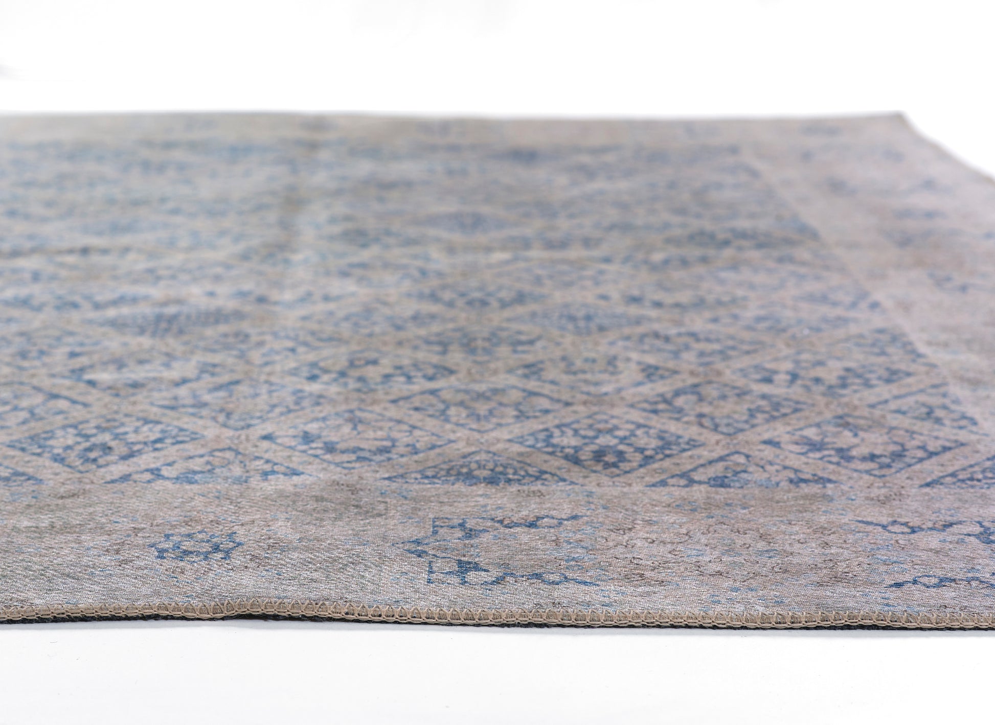 Rectangular rug with blue geometric diamond motifs on a beige-gray background; low-pile, flat-weave style.