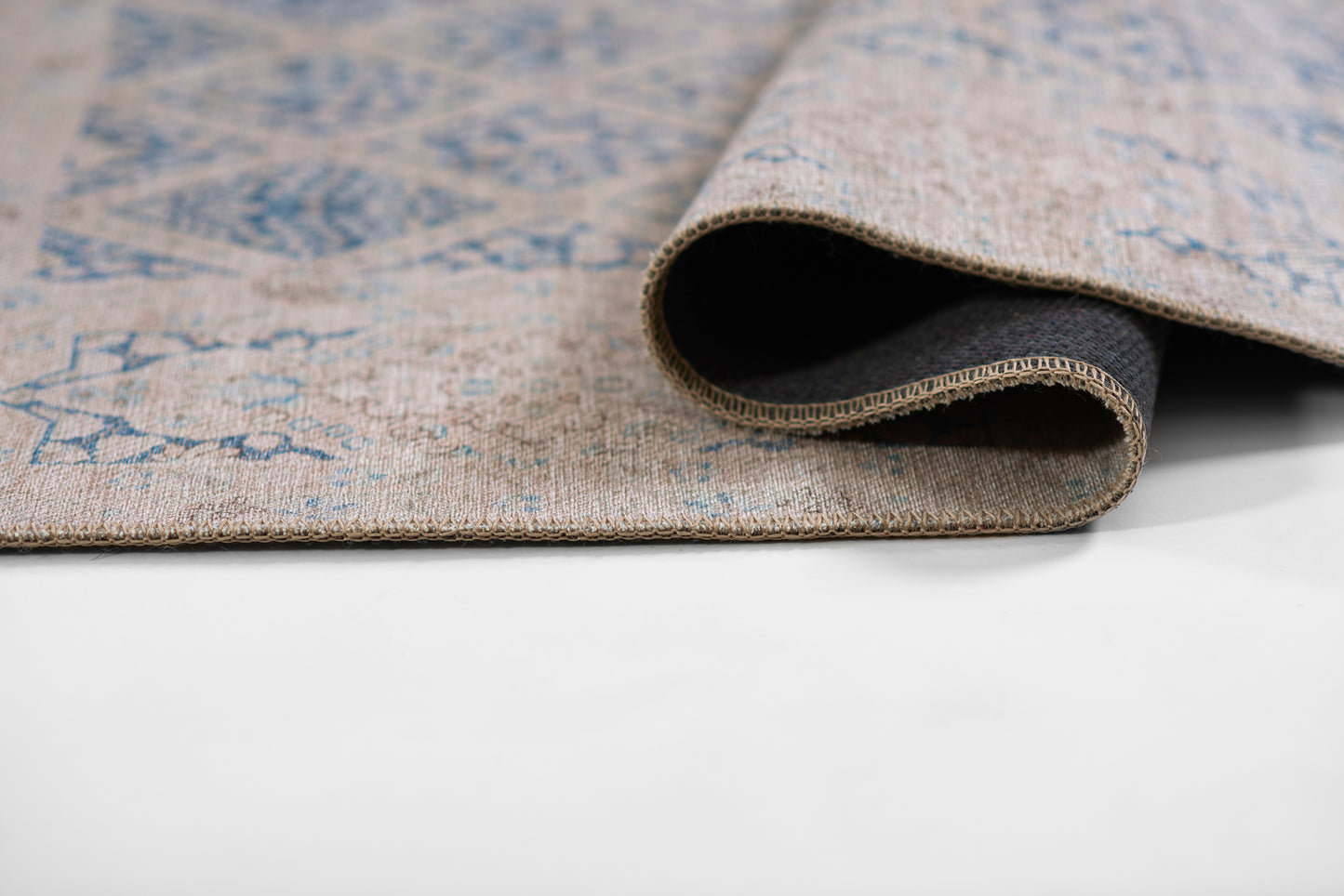 Beige-blue woven rug with blue geometric pattern, rolled edge shows thickness; natural fiber, cozy living room mat.