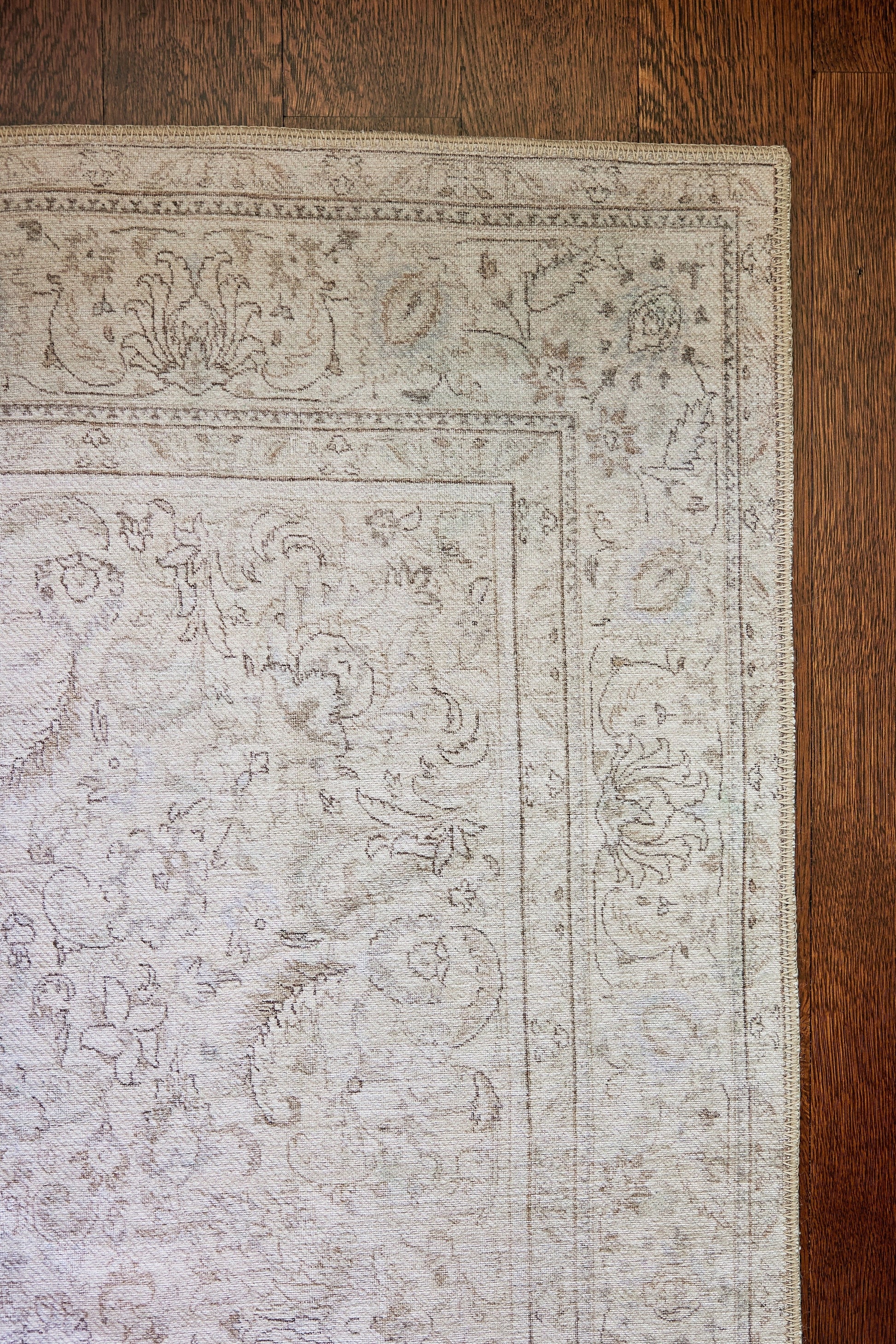 Rectangular soft gray traditional rug with delicate floral border on a dark wood floor.