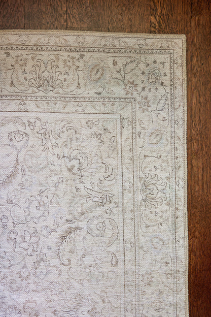 Light gray oriental-style rug with a delicate floral border pattern on a dark wooden floor.