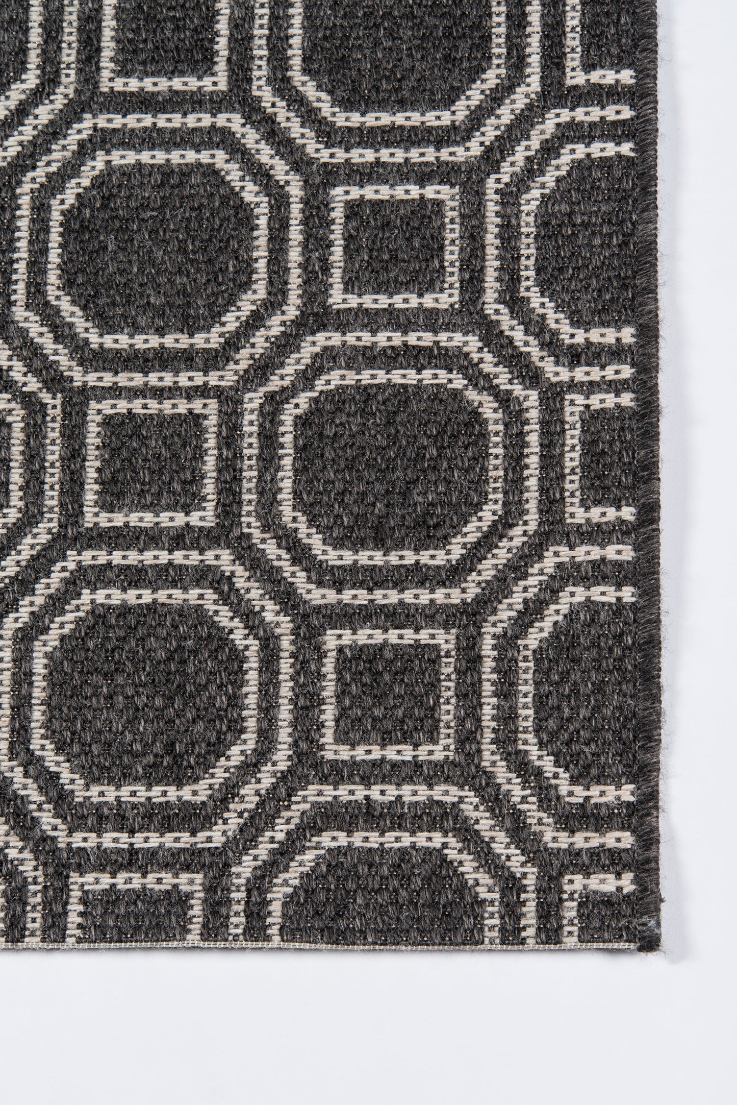 Charcoal rug with white geometric outlines forming interlocking rounded-square and octagon shapes; modern textured pattern.