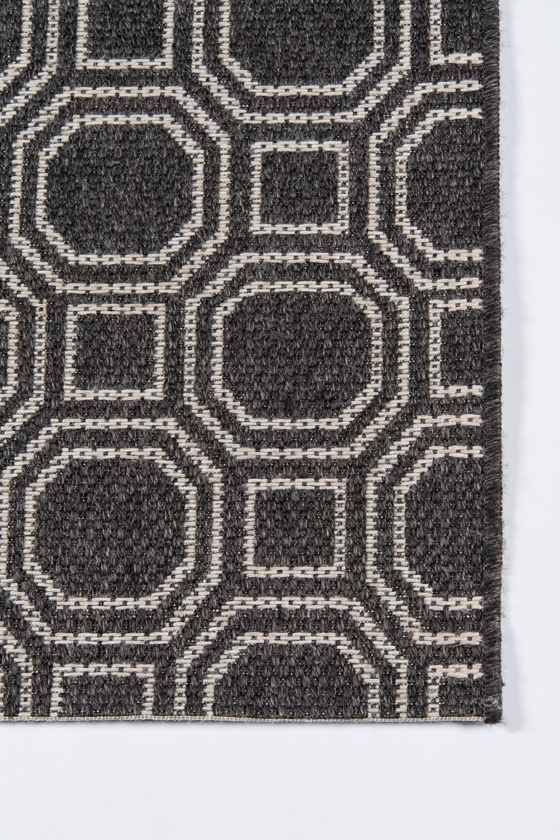 Charcoal rug with white geometric outlines forming interlocking rounded-square and octagon shapes; modern textured pattern.