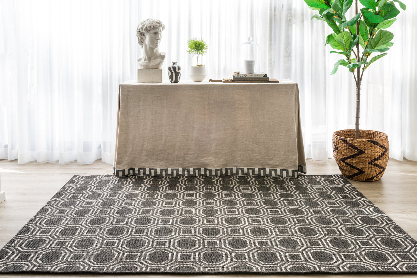 Dark gray geometric rug with white interlocking circle pattern, placed in a bright room beside a beige table and greenery.