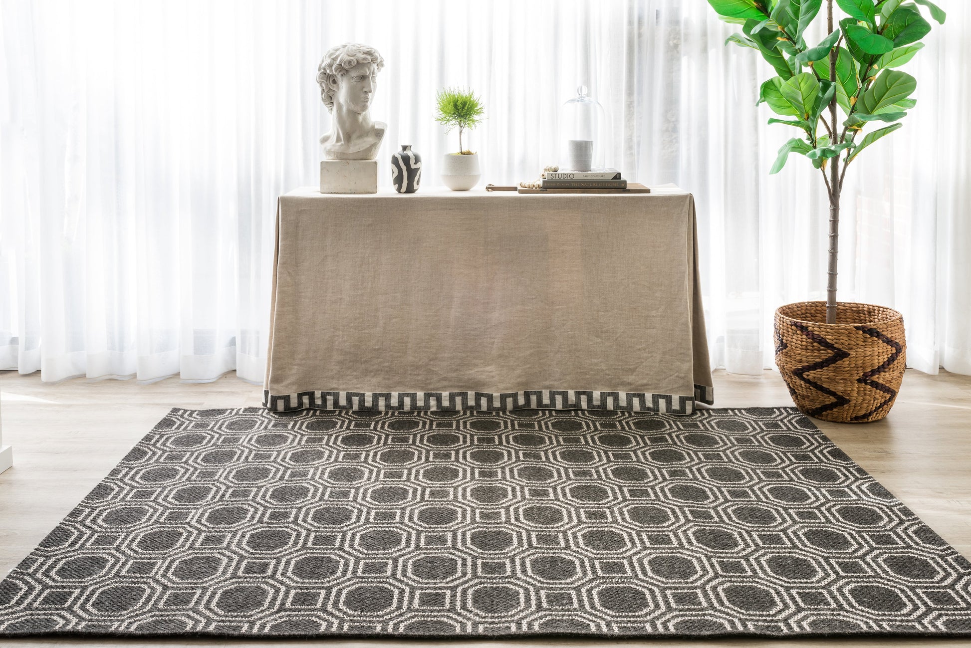 Dark gray geometric rug with white interlocking circle pattern, placed in a bright room beside a beige table and greenery.