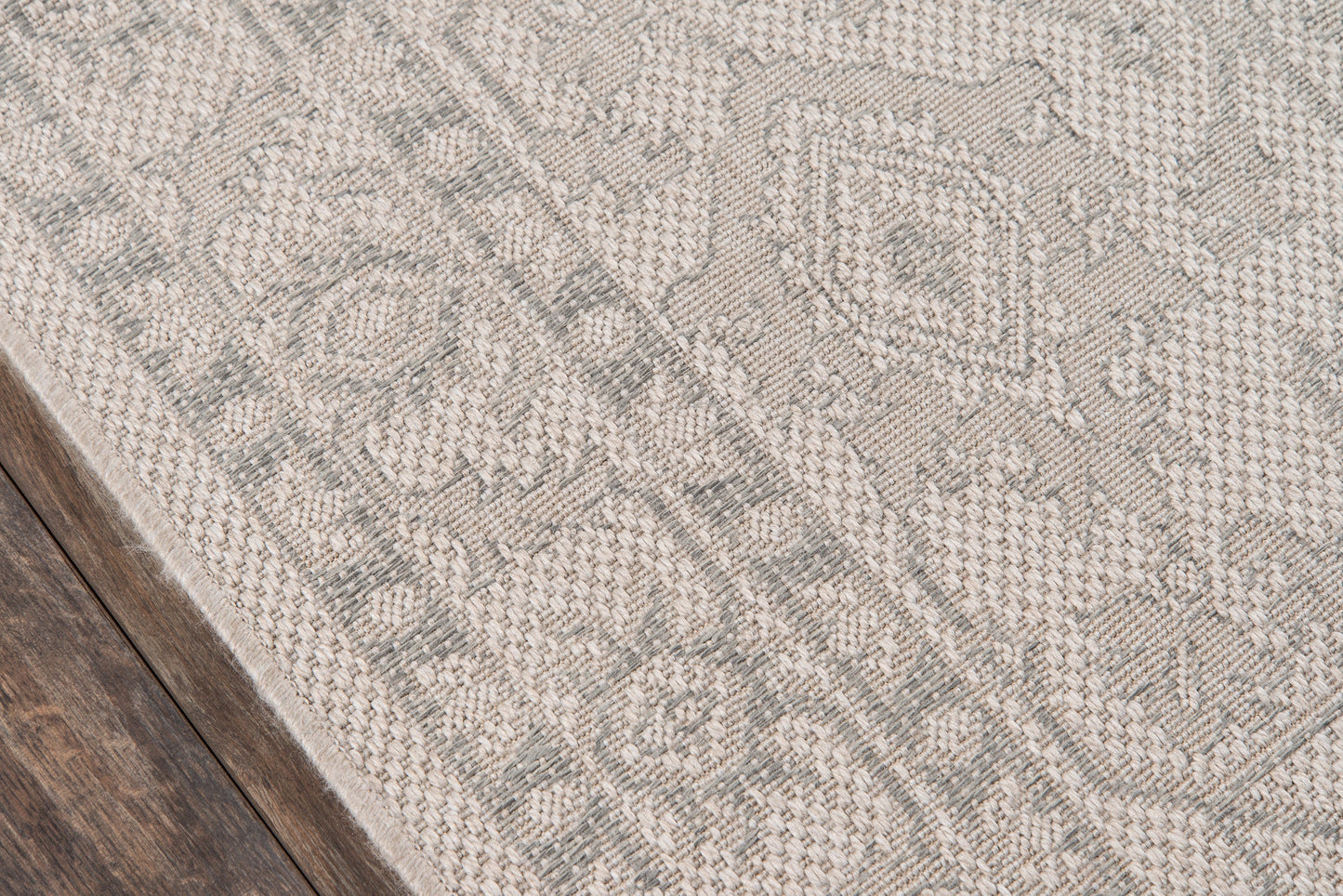 Corner view of a gray woven patterned runner with ornate motifs on dark wood floor.