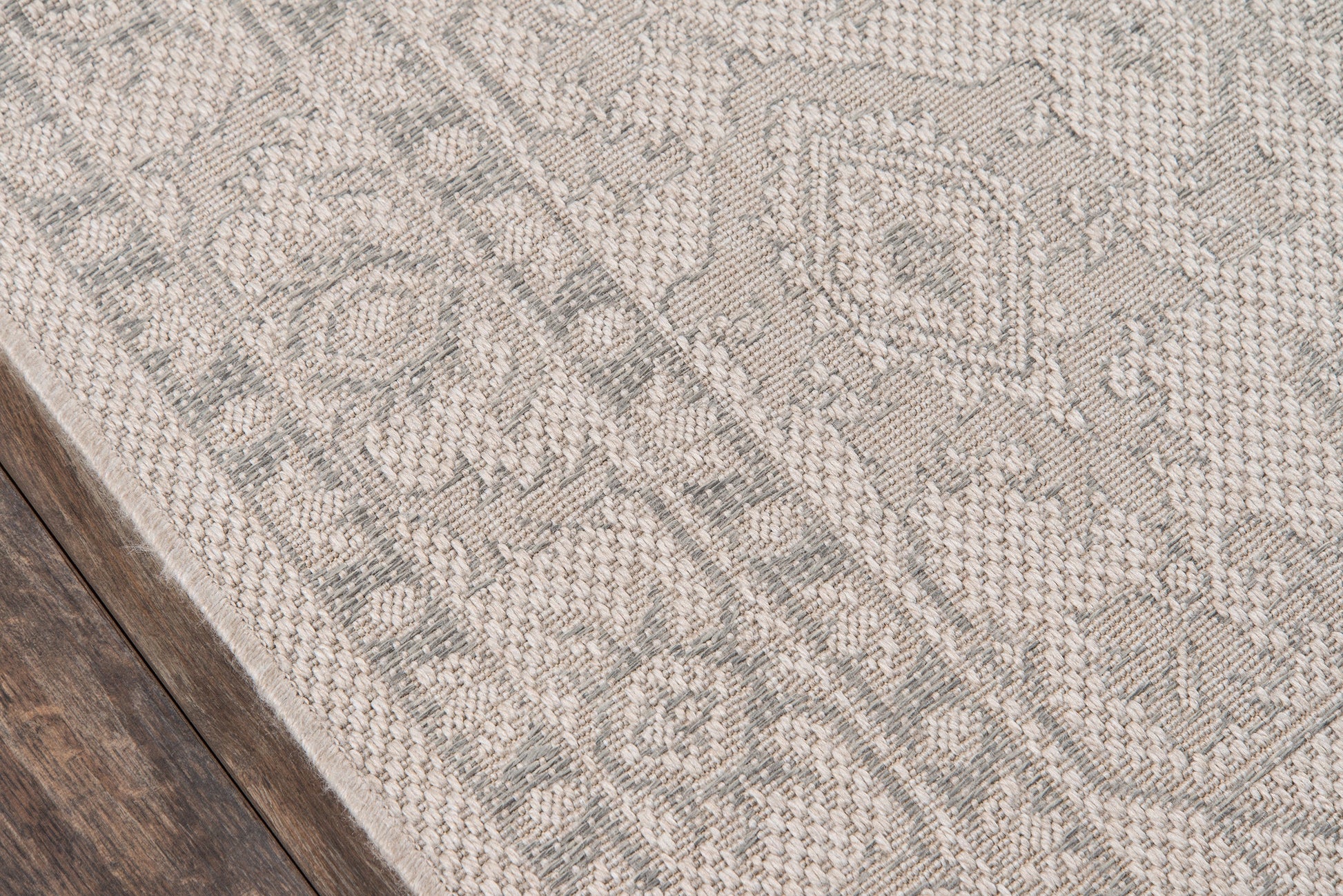 Corner view of a gray woven patterned runner with ornate motifs on dark wood floor.