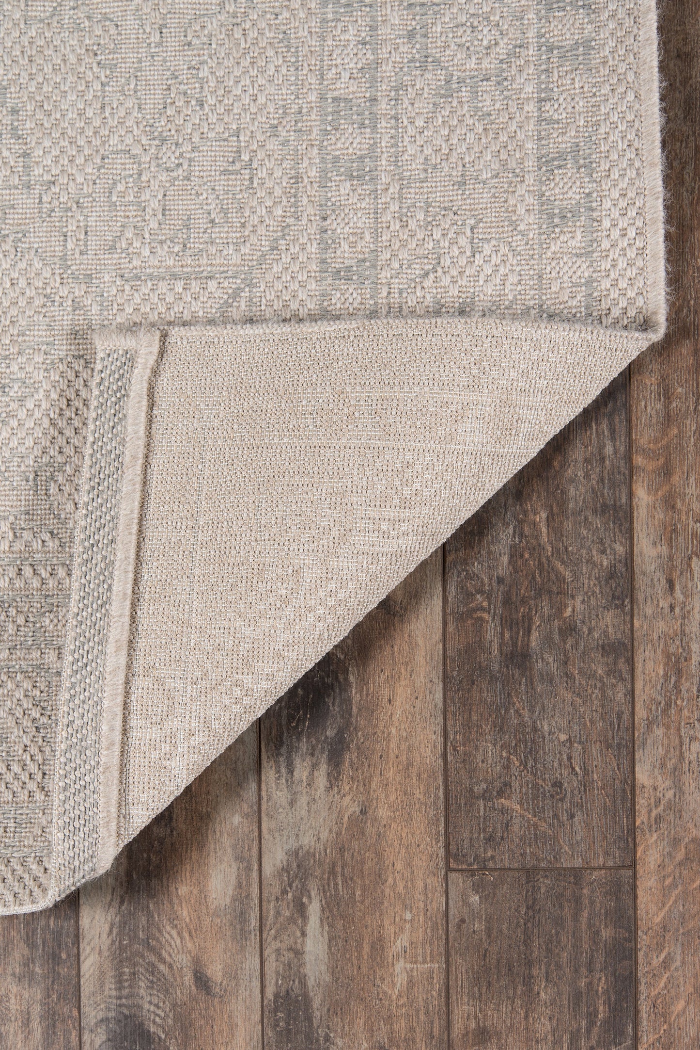 Rectangular beige-gray woven rug with subtle geometric pattern, folded corner on dark wood floor.