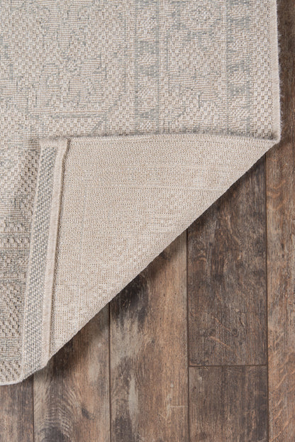 Rectangular beige-gray woven rug with subtle geometric pattern, folded corner on dark wood floor.