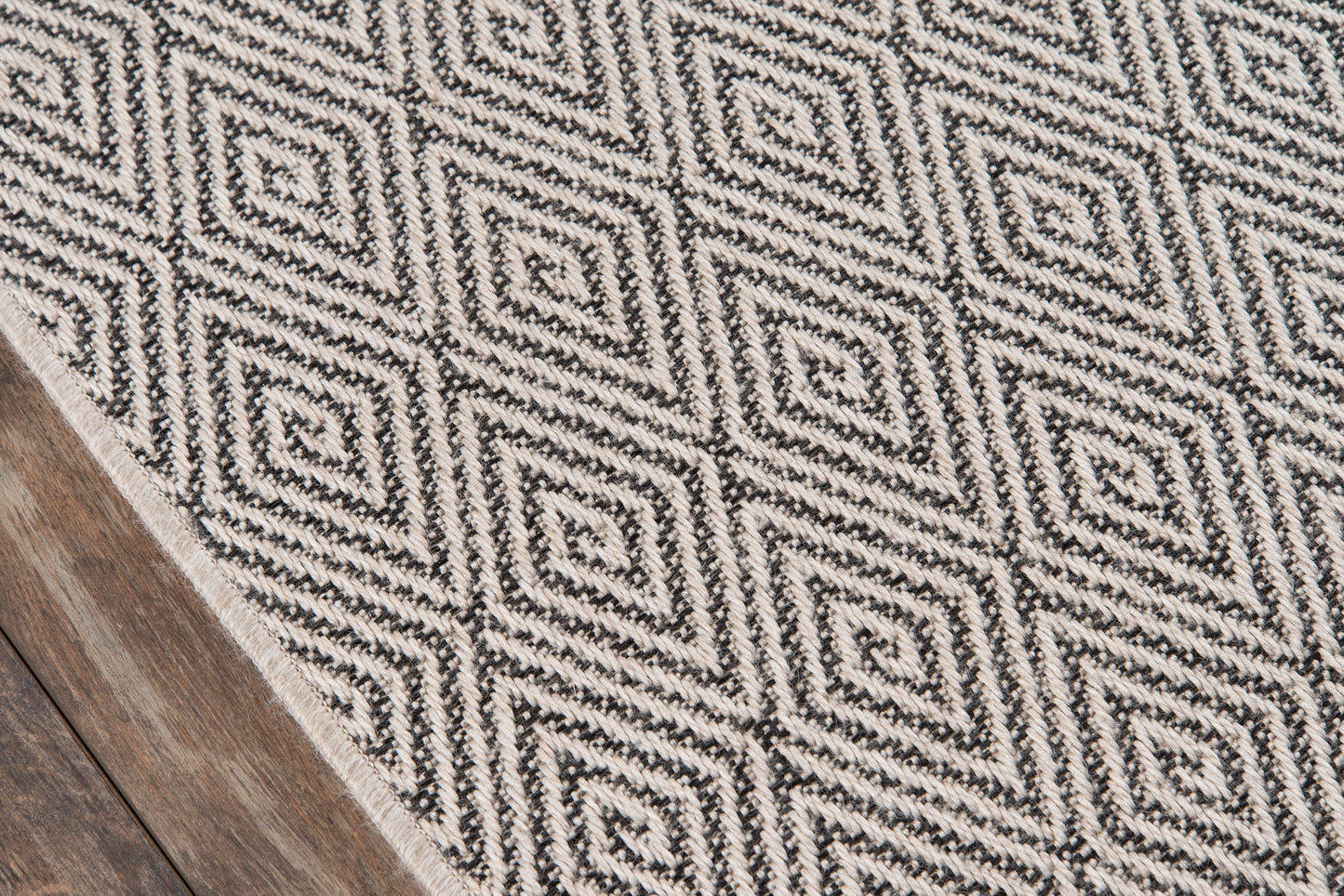 Ivory flat-weave rug with black diamond geometric pattern on a wooden floor.