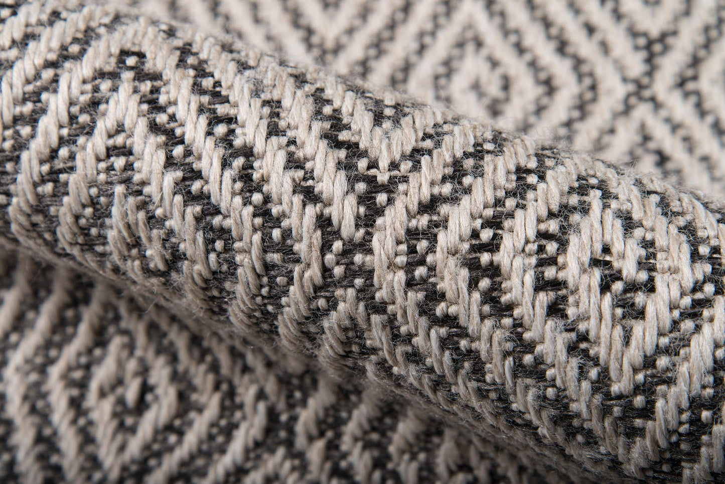 Close-up of gray and black woven fabric with a chevron/herringbone pattern and chunky yarns; rug material.