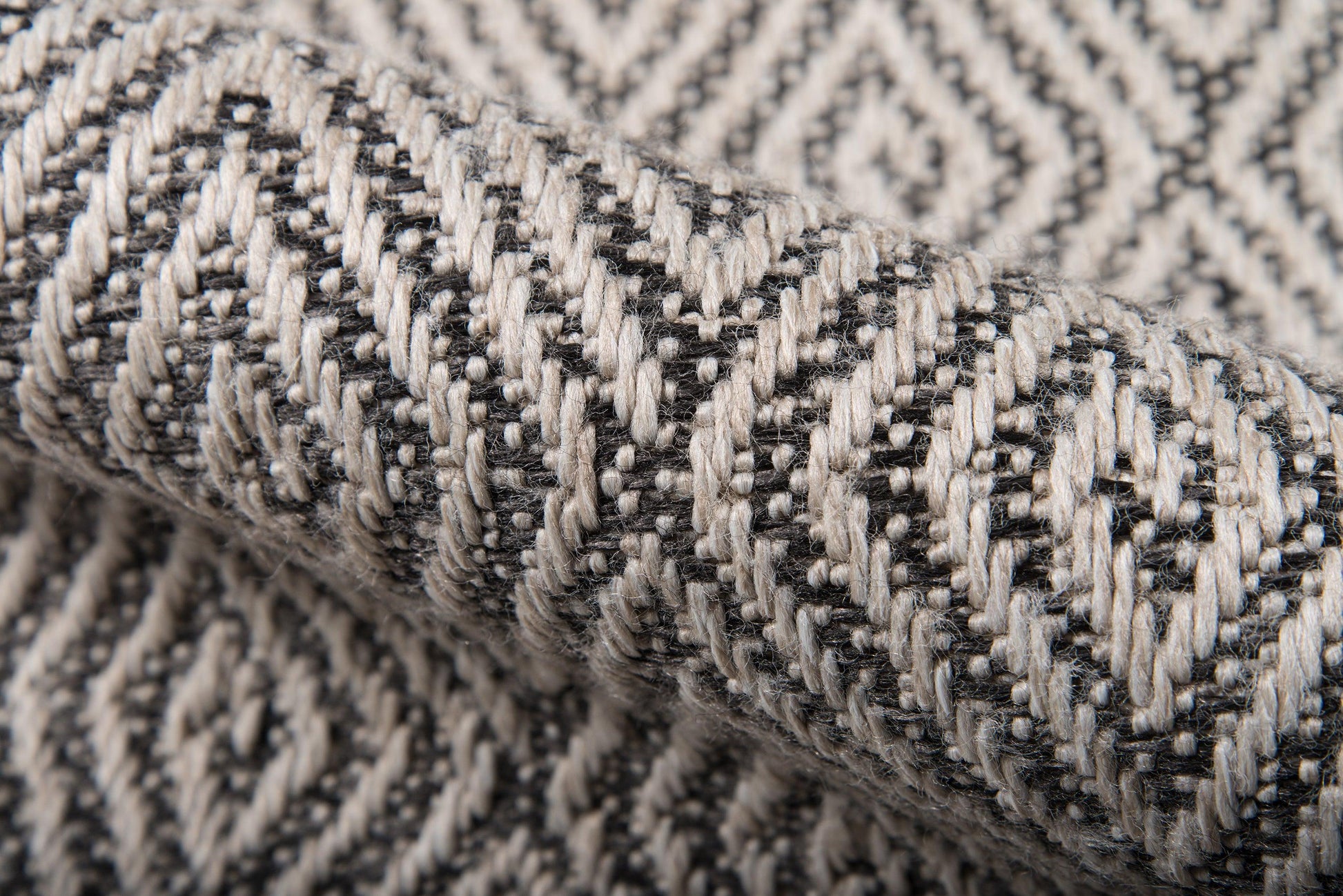 Close-up of gray and black woven fabric with a chevron/herringbone pattern and chunky yarns; rug material.