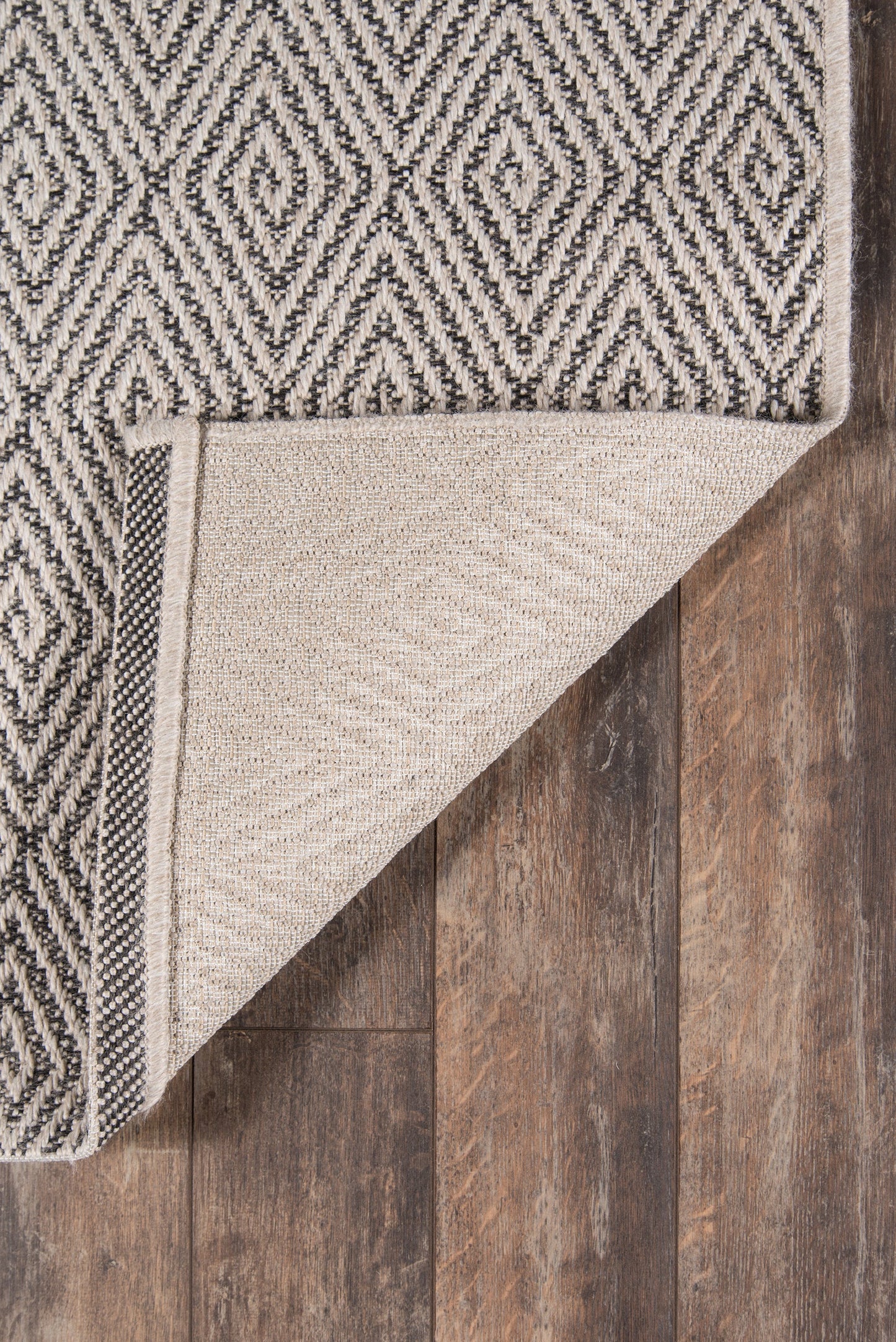 Two-tone geometric runner rug with black and white diamond pattern, folded corner reveals beige underside, on dark wood floor.