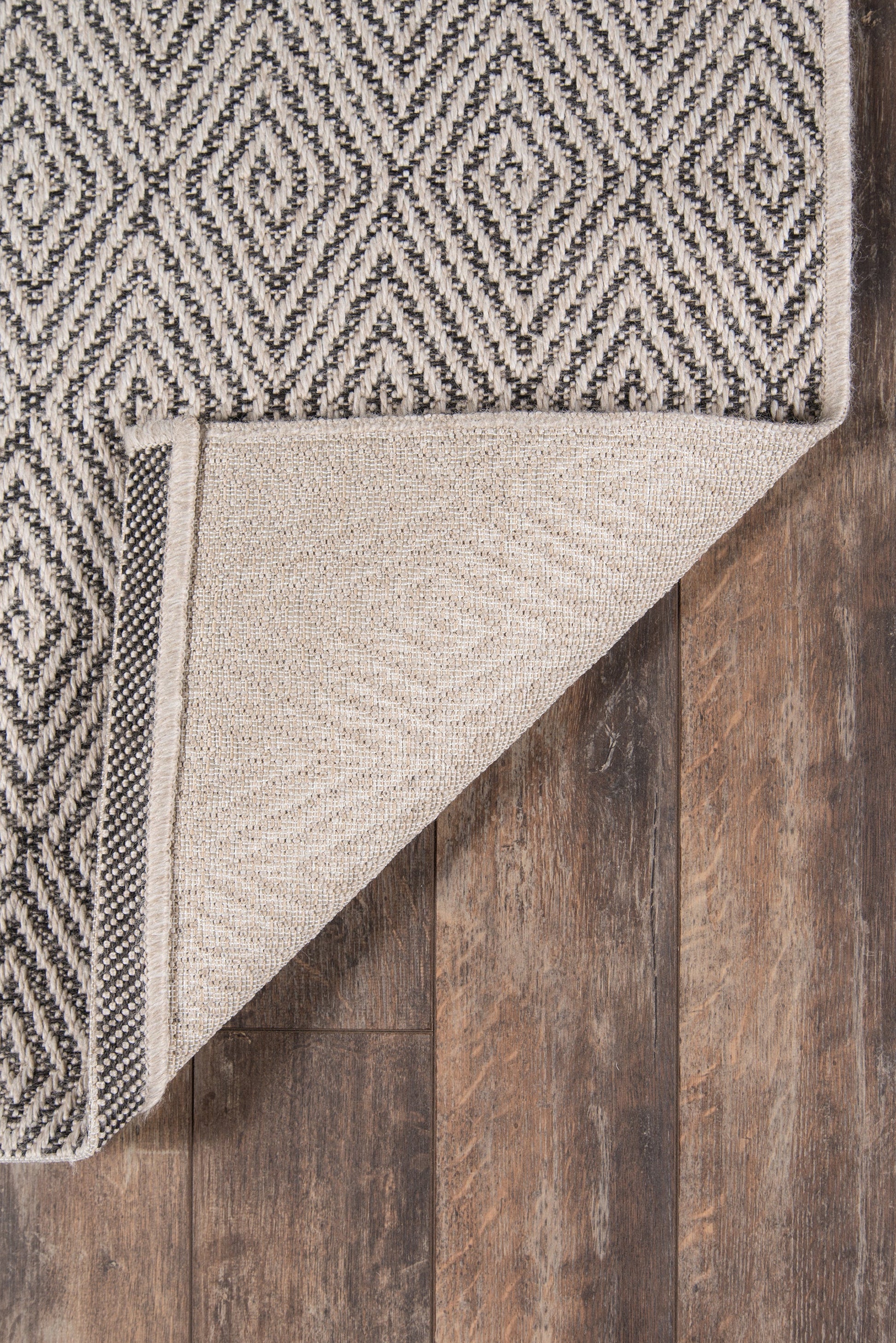 Two-tone geometric runner rug with black and white diamond pattern, folded corner reveals beige underside, on dark wood floor.