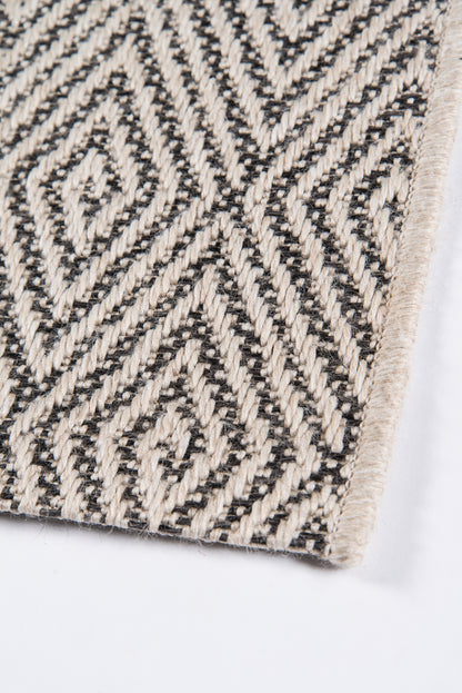 Beige and black woven rug with geometric diamonds and chevrons and a cream fringe along the edge.