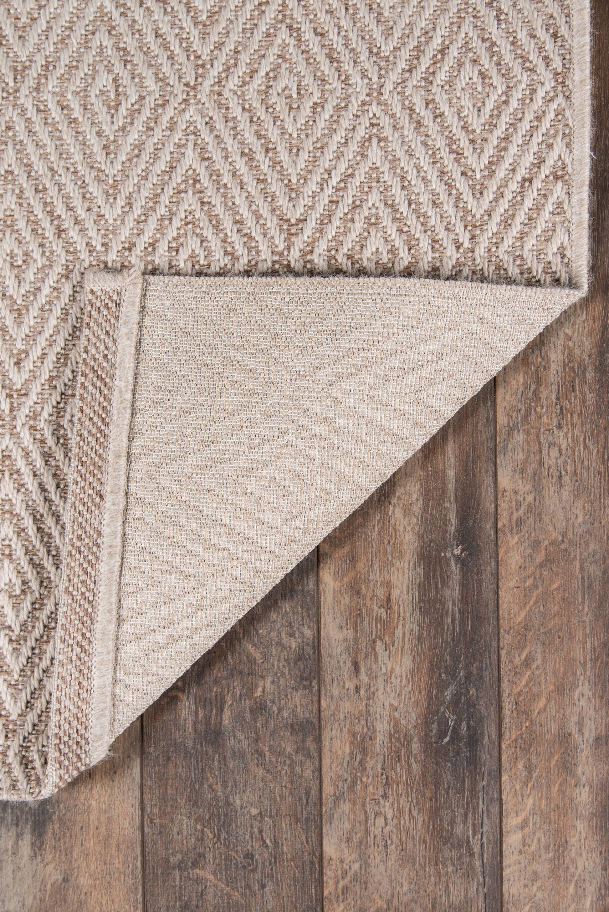 Beige geometric diamond woven rug with natural fibers; folded corner reveals underside on dark wood floor.