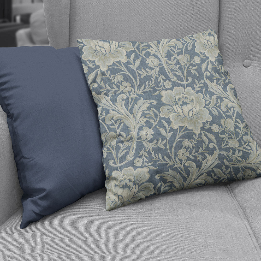 Two cushions on a gray sofa: solid navy pillow beside a blue damask floral-patterned cushion with cream accents.