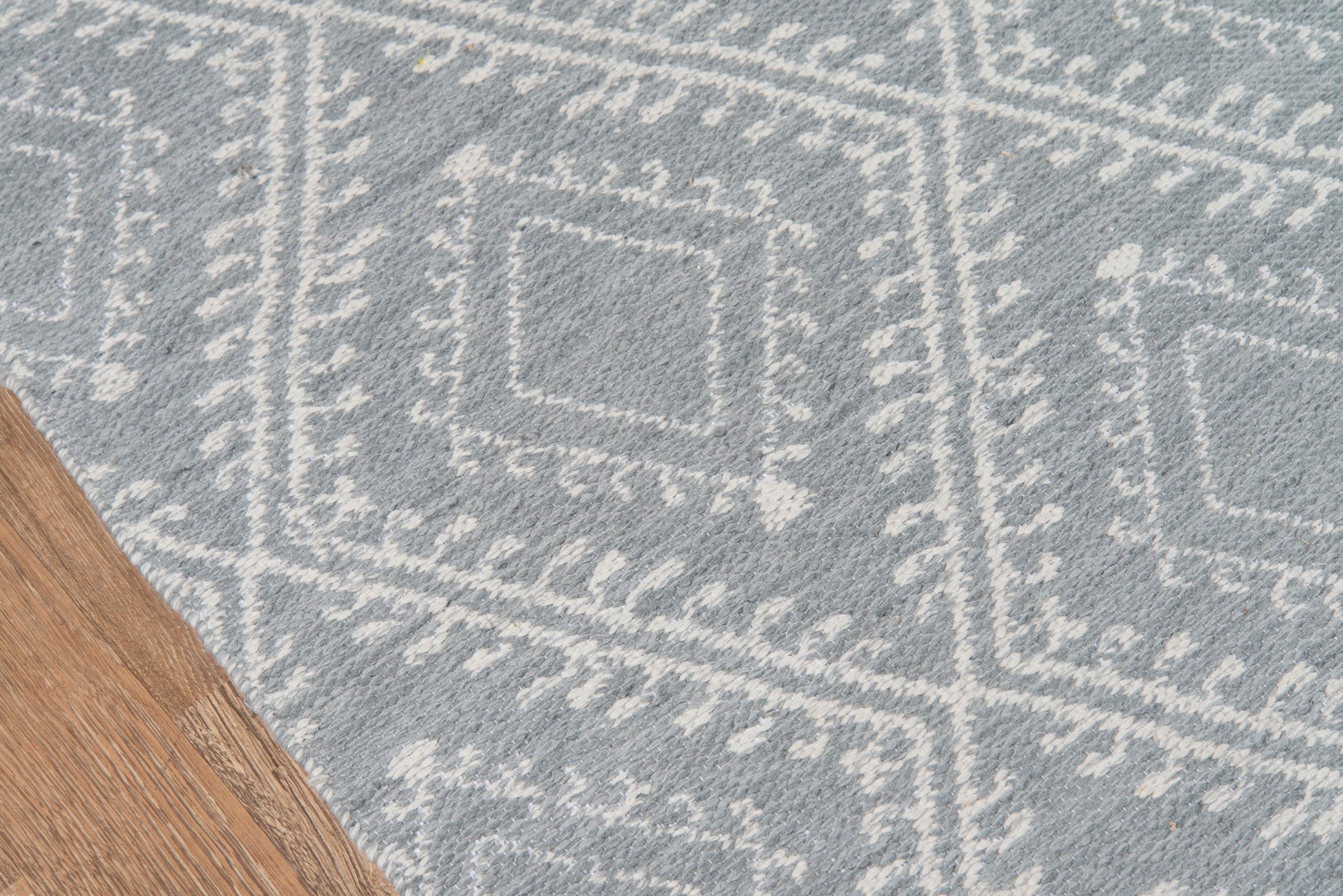 Gray rug with white geometric diamond pattern and border details; wood floor edge visible.