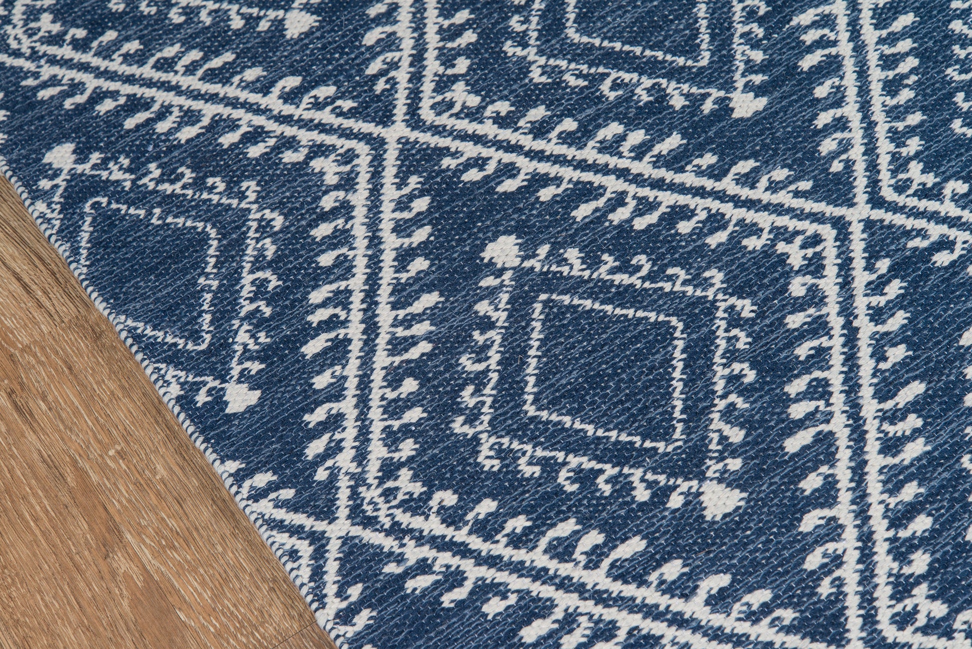 Navy blue rug with white diamond-square motifs and bordered frames; woven textile with a folded edge on wood floor.