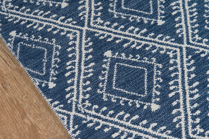 Navy blue rug with white diamond-square motifs and bordered frames; woven textile with a folded edge on wood floor.