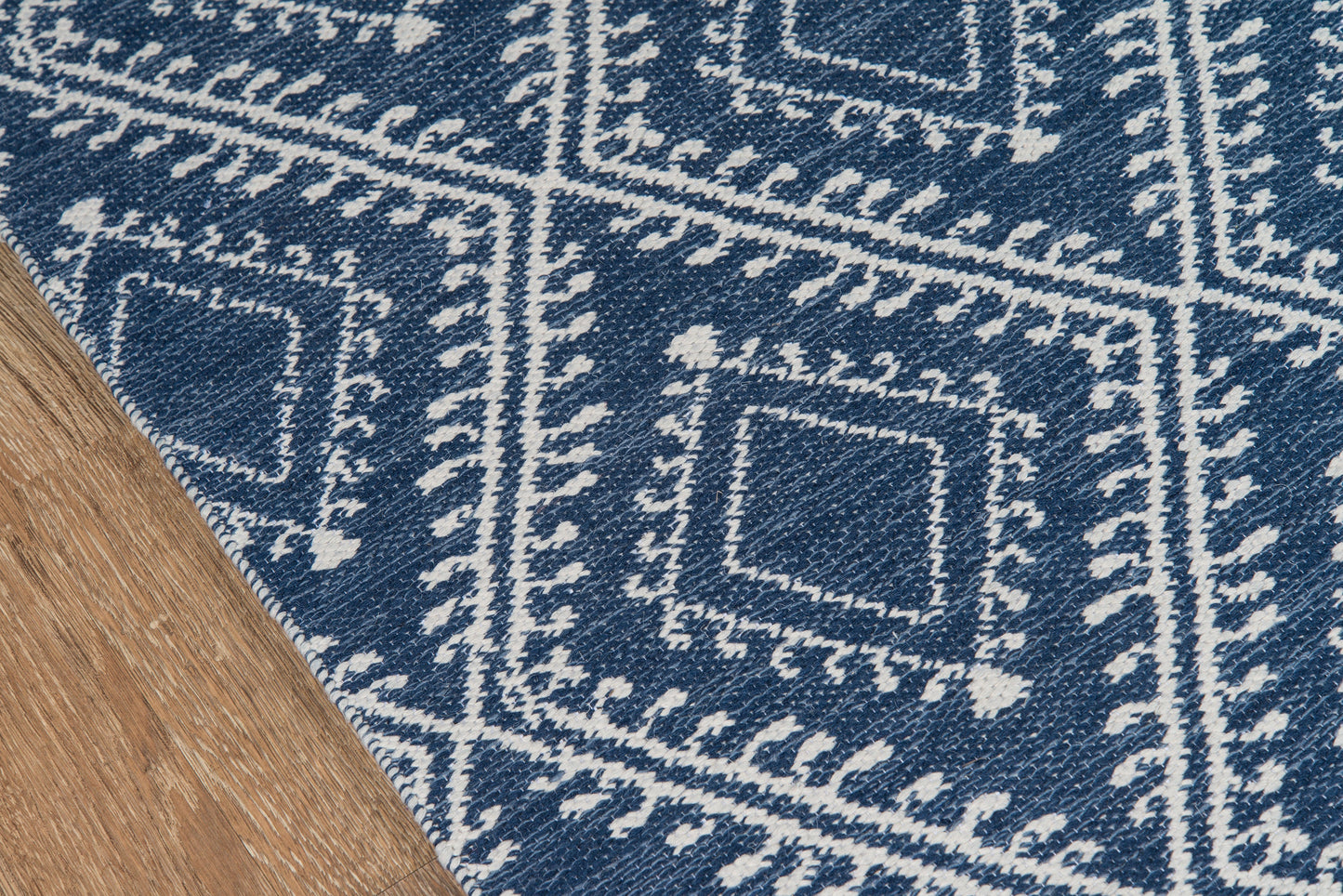 Navy blue woven rug with white geometric square motifs on wood floor; textured, kilim-style pattern.