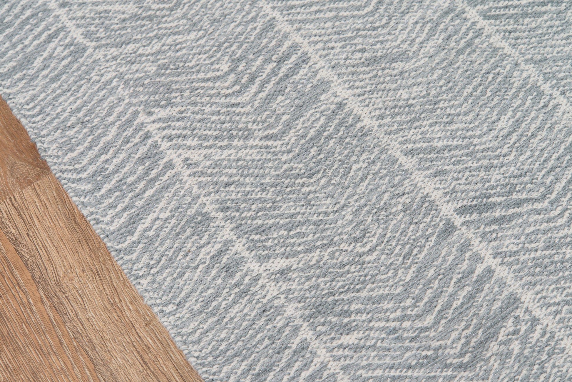 Rectangular gray woven rug with chevron pattern on wood floor; modern textured geometric style.