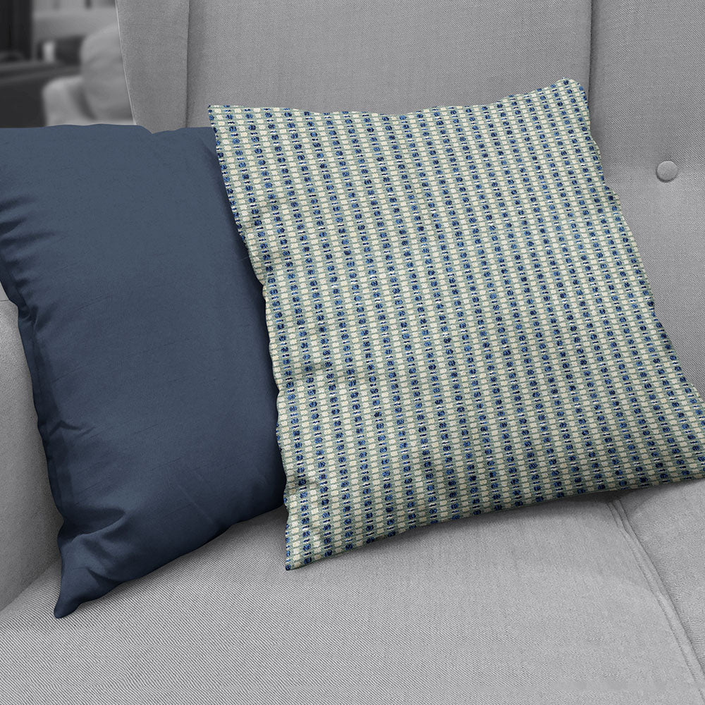 Two decorative throw pillows on a gray upholstered sofa, made with Ink Stripe fabric: one solid navy, the other a blue-beige geometric woven pattern.