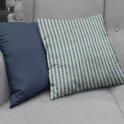 Two decorative throw pillows on a gray upholstered sofa, made with Ink Stripe fabric: one solid navy, the other a blue-beige geometric woven pattern.