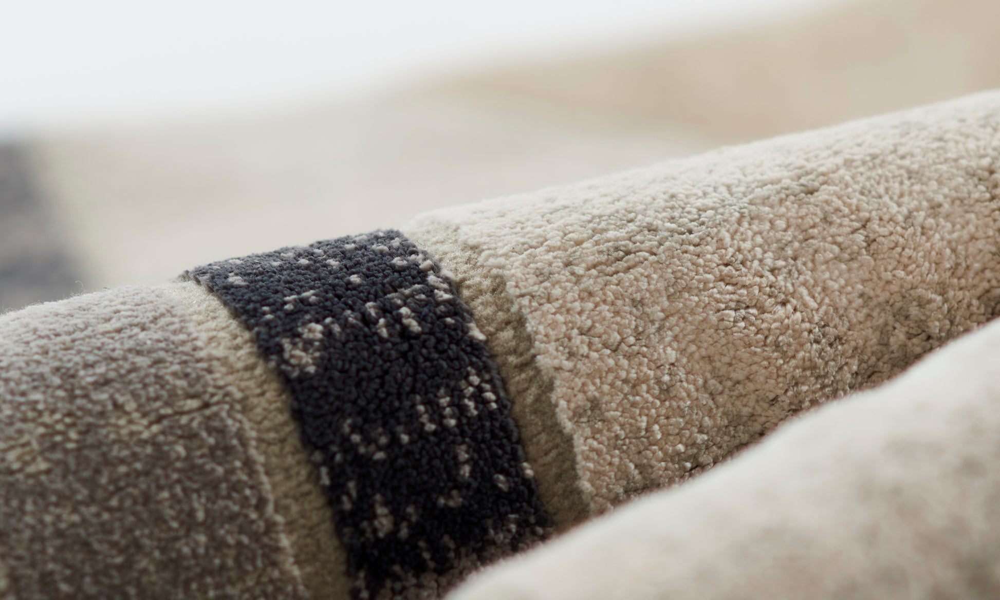 Close-up of beige plush rug with a dark charcoal stripe, textured pile, rolled.
