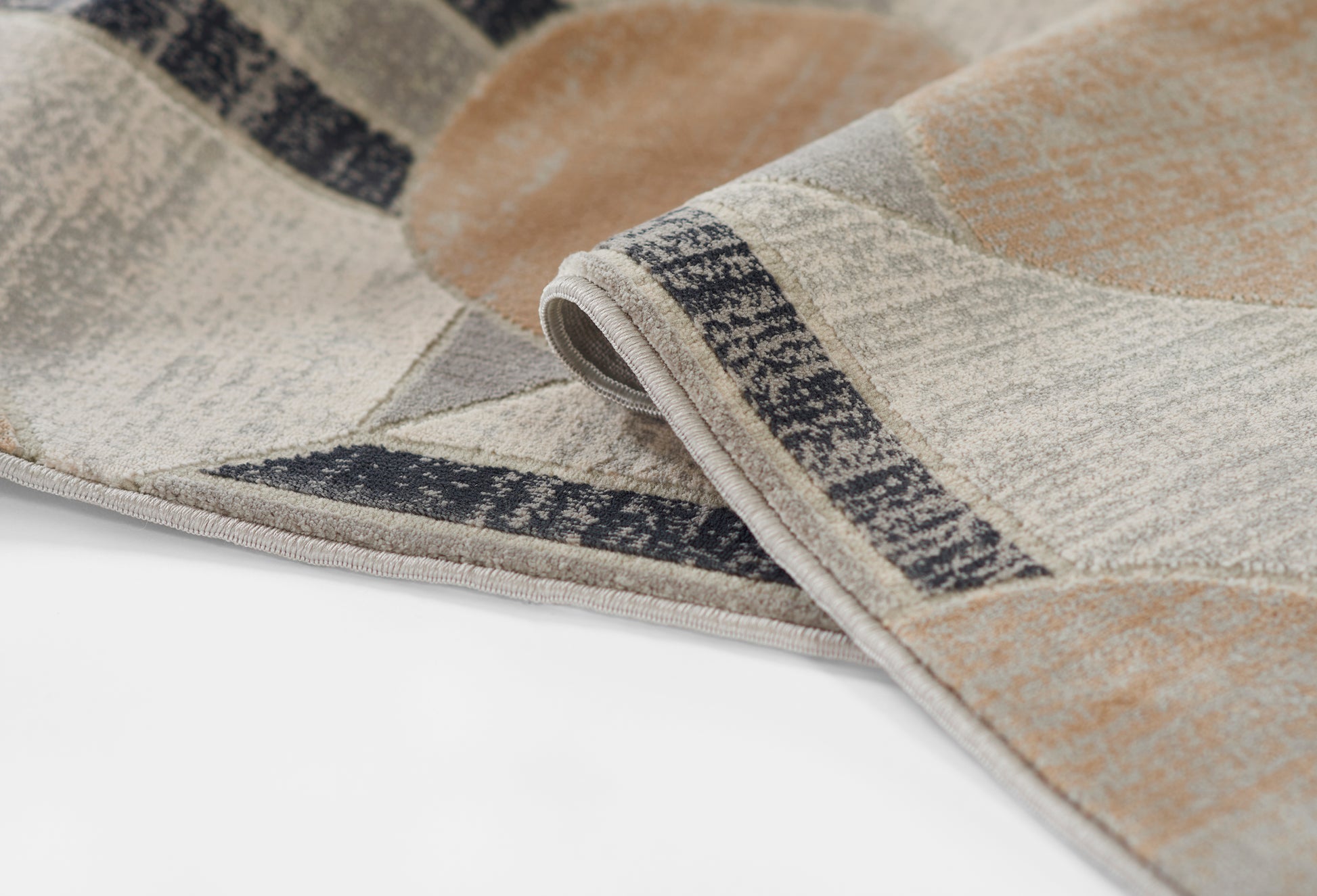 Geometric patterned woven rug in beige, taupe, ivory and gray with a dark border; folded corner detail.