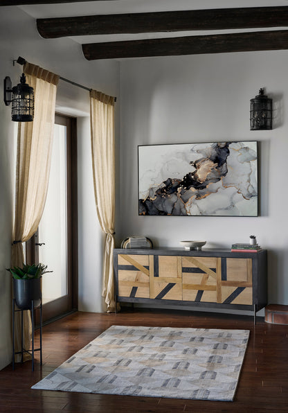 Living room corner with dark wood beams, beige curtains, a geometric wood cabinet, marble art, lantern sconces, plant, and rug.