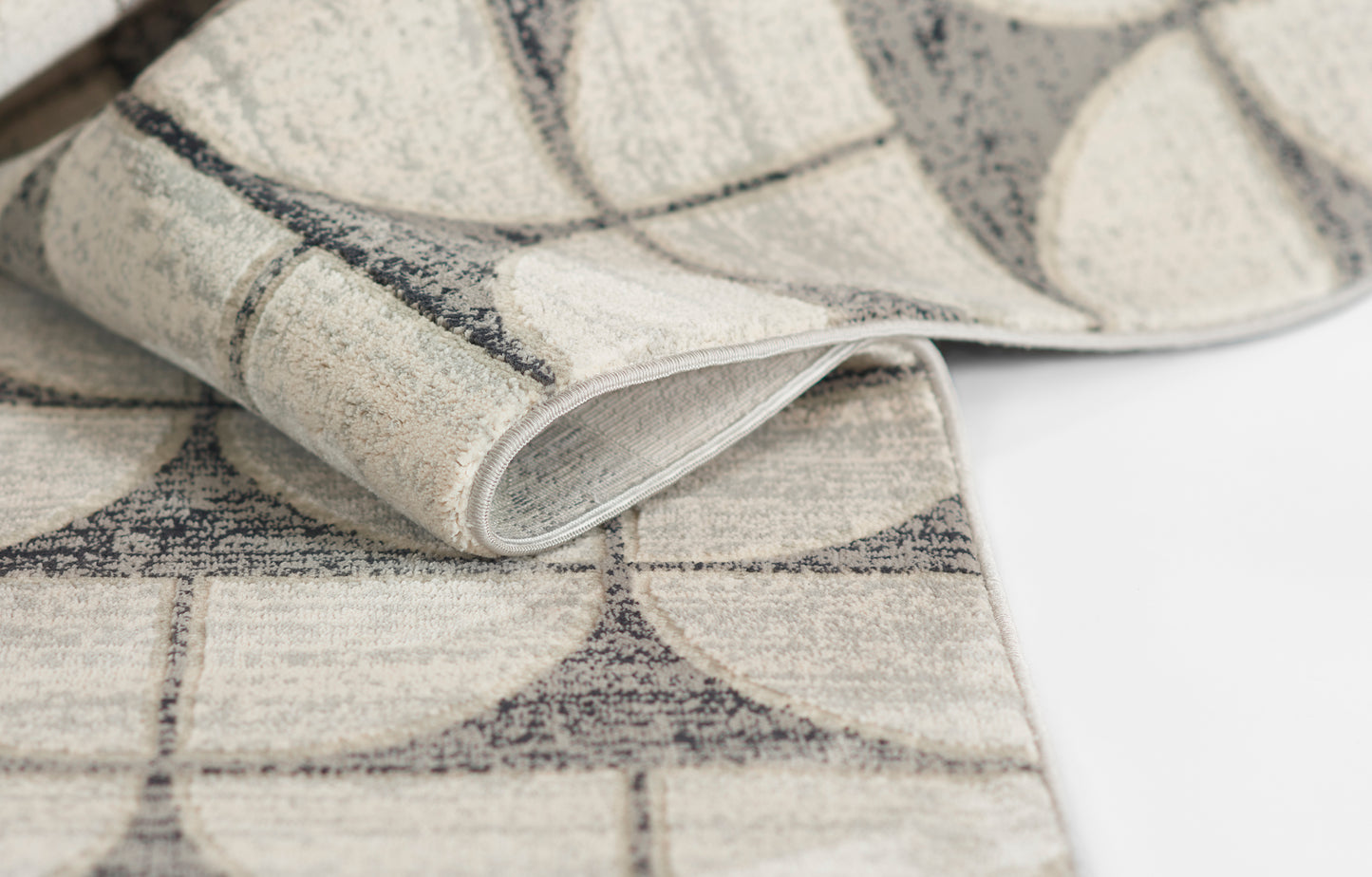 Beige and gray woven rug with curved circular arc pattern and rolled edge.