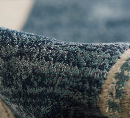 Close-up of a dense blue textured rug with dark and light blue fibers and a beige border.