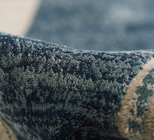 Close-up of a dense blue textured rug with dark and light blue fibers and a beige border.