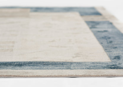 Close-up of a beige area rug with a blue border and modern geometric edge, soft woven texture.
